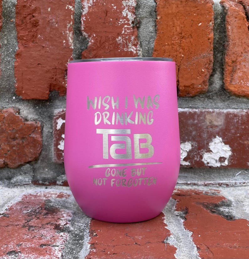 Op de afbeelding: Een felroze ge&iuml;soleerde tumbler met zilverkleurige tekst. De tekst luidt "WISH I WAS DRINKING TAB", met "TAB" in een groot lettertype en daaronder "GONE BUT NOT FORGOTTEN".