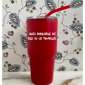 Op de afbeelding: Een rode beker van 887 ml met een rood rietje. De beker heeft een zilveren deksel en de tekst "ALSO AVAILABLE AS RED 30 OZ TUMBLER". De achtergrond heeft een bloemenpatroon met blauwe en bruine bladeren.