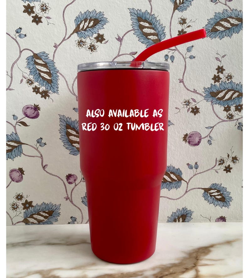 Op de afbeelding: Een rode beker van 887 ml met een rood rietje. De beker heeft een zilveren deksel en de tekst "ALSO AVAILABLE AS RED 30 OZ TUMBLER". De achtergrond heeft een bloemenpatroon met blauwe en bruine bladeren.