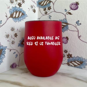 Op de afbeelding: Een helderrode 355 ml tumbler met een afgeronde basis. De tekst "ALSO AVAILABLE AS RED 12 OZ TUMBLER" staat in het wit. De tumbler staat tegen een bloemig patroon.