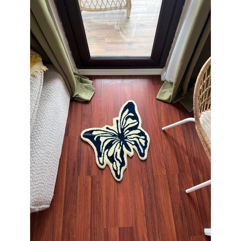 May include: A cream-colored rug with a dark blue butterfly design. The rug is on a hardwood floor.