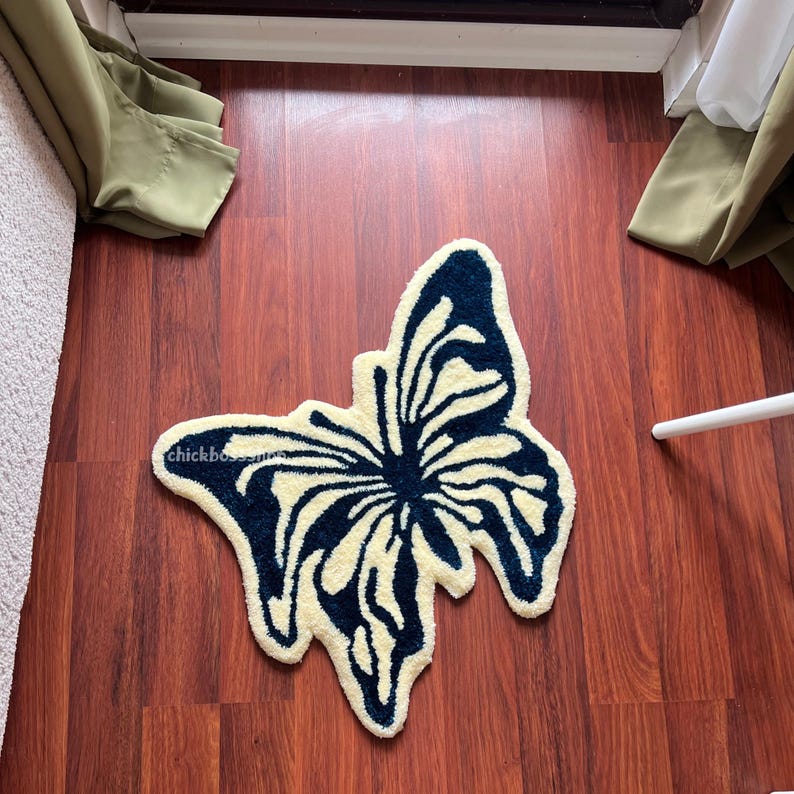 May include: A cream-colored butterfly rug with dark blue accents. The rug is made of soft, plush material and features a realistic butterfly design.
