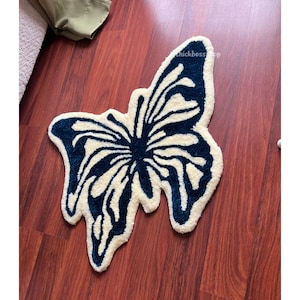 May include: A white and blue butterfly-shaped rug with a fluffy texture. The rug is on a wooden floor.
