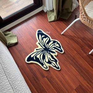 May include: A cream-colored rug shaped like a butterfly with dark blue accents. The rug is on a wooden floor.