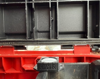 May include: A black and red plastic storage container with a black OWR-branded component attached. The component has a circular lens. The container has multiple compartments.