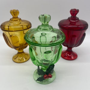 May include: Three glass candy dishes with lids. The dishes are in amber, green, and red. The green dish has a holly and berry design on the base.