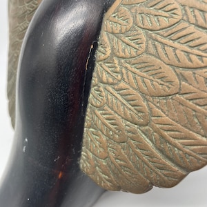 Puede incluir: Una escultura de madera de un p&aacute;jaro con alas de bronce. Las alas est&aacute;n detalladas con un patr&oacute;n de hojas.