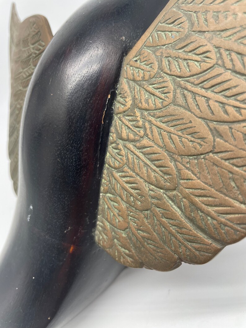 Puede incluir: Una escultura de madera de un p&aacute;jaro con alas de bronce. Las alas est&aacute;n detalladas con un patr&oacute;n de hojas.