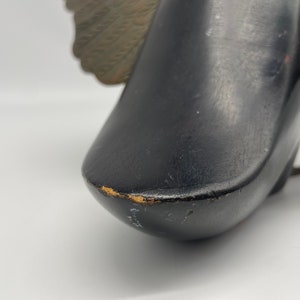 Puede incluir: Figurita de p&aacute;jaro de madera negra con alas doradas. El p&aacute;jaro est&aacute; mirando hacia la derecha y tiene un acabado liso y pulido.