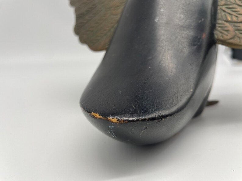Puede incluir: Figurita de p&aacute;jaro de madera negra con alas doradas. El p&aacute;jaro est&aacute; mirando hacia la derecha y tiene un acabado liso y pulido.