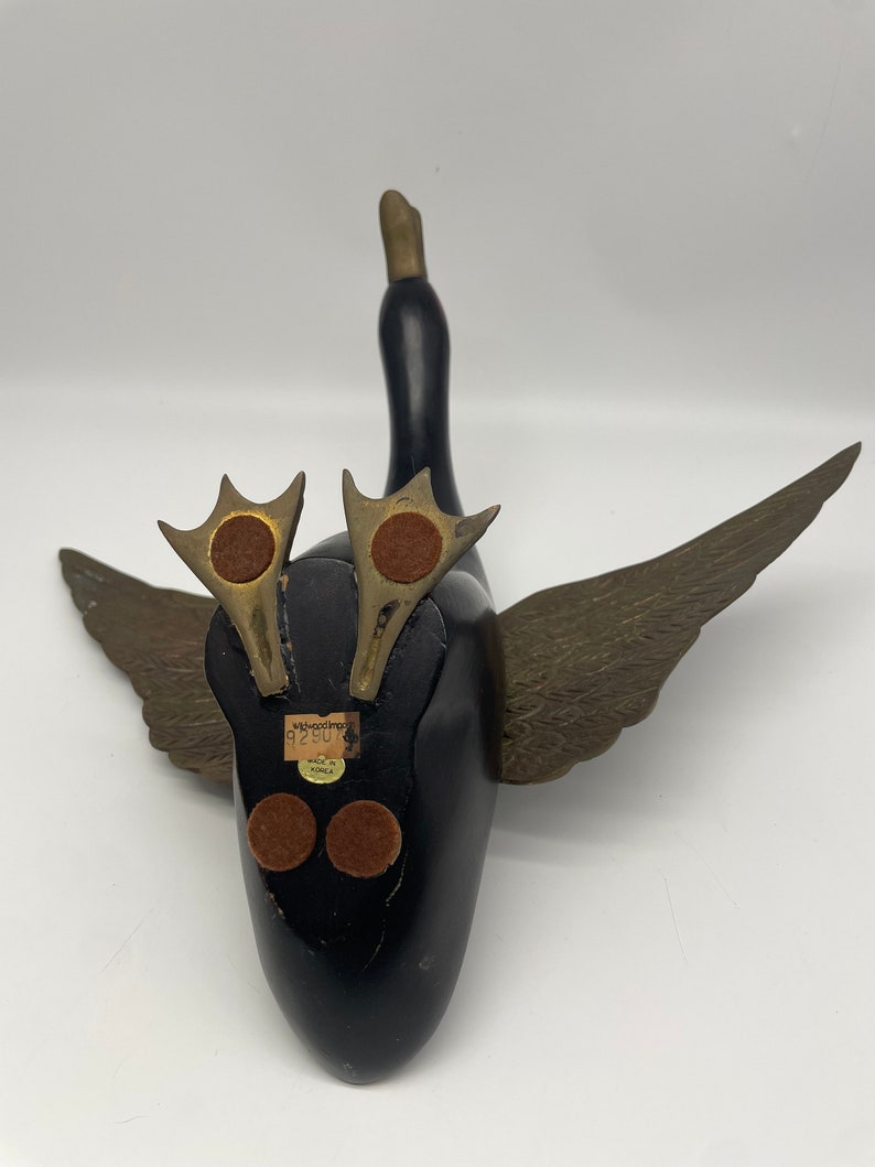 Puede incluir: Figurita de pato de madera negra con alas doradas y una etiqueta que dice "Wood Imports 92807 Made in Korea".