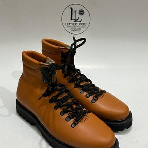 May include: A pair of tan leather hiking boots with black laces and soles. The boots have a classic design with metal eyelets and a padded collar. The boots are new and unworn.