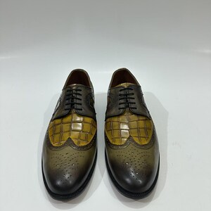 Puede incluir: Un par de zapatos oxford con un dise&ntilde;o bicolor que presenta un empeine de cuero con relieve de cocodrilo en color amarillo mostaza y una puntera y tal&oacute;n de cuero bru&ntilde;ido en verde oliva oscuro. Incluyen cordones negros y detalles brogue.