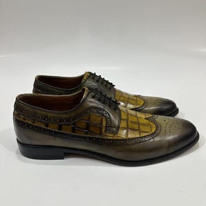 Puede incluir: Un par de zapatos oxford de cuero en color verde oliva y amarillo mostaza con dise&ntilde;o brogue wingtip, textura de cuadr&iacute;cula en los paneles laterales, cordones negros y un acabado degradado marr&oacute;n oscuro en la punta y el tal&oacute;n.