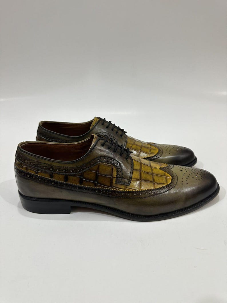 Puede incluir: Un par de zapatos oxford de cuero en color verde oliva y amarillo mostaza con dise&ntilde;o brogue wingtip, textura de cuadr&iacute;cula en los paneles laterales, cordones negros y un acabado degradado marr&oacute;n oscuro en la punta y el tal&oacute;n.