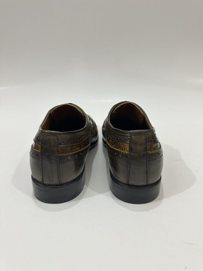 Puede incluir: Un par de zapatos de vestir de cuero gris oscuro con un panel texturizado con relieve de cocodrilo en los laterales y el tal&oacute;n. Los zapatos tienen un borde perforado estilo brogue, un tac&oacute;n bajo y un acabado liso y pulido.