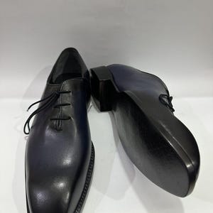 May include: A pair of dark blue and black leather oxford shoes with a smooth finish, featuring a rounded toe, black laces, and a low stacked heel. The shoes are positioned with one facing forward and the other showing the smooth black sole.