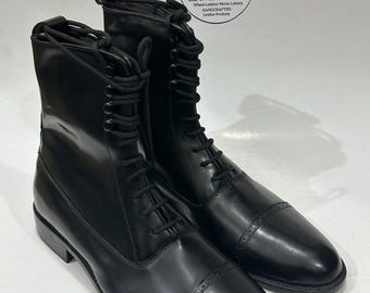May include: A pair of black leather lace-up boots featuring a cap toe with decorative perforations, black laces, and a pull tab at the heel. A circular logo in the background displays the text LEATHER LORDS Where Leather Meets Luxury.
