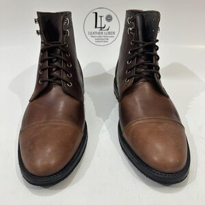 May include: A pair of brown leather lace-up boots with cap toes, silver-toned metal eyelets, and black soles. A circular logo with the text LEATHER LORDS is positioned between the boots, featuring a stylized LL monogram and text.