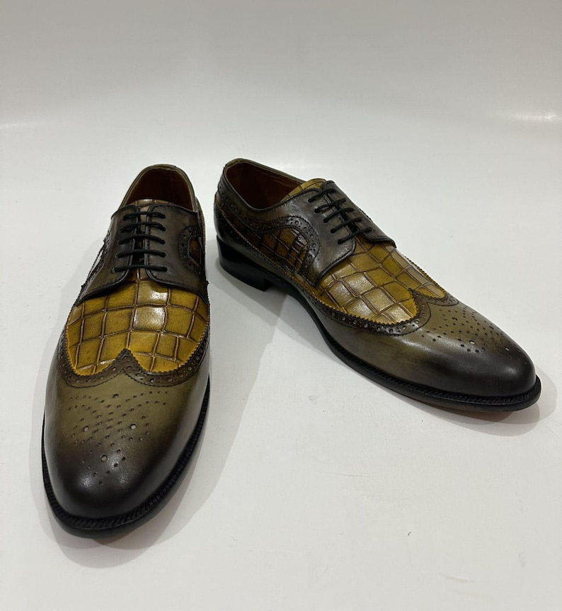 Puede incluir: Un par de zapatos oxford tipo wingtip con dise&ntilde;o bicolor, que presenta un empeine de cuero color amarillo mostaza con relieve de cocodrilo y detalles en cuero verde oliva oscuro. Incluyen cordones negros, detalles brogue y tac&oacute;n bajo.
