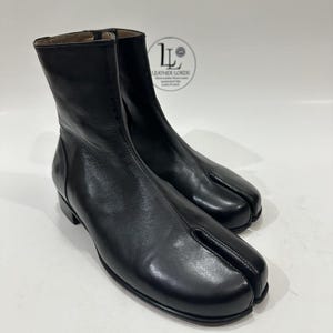 Op de afbeelding: Zwarte leren enkellaarsjes met een split-teen ontwerp. De laarzen hebben een rits aan de binnenkant en een lage hak. Het Leather Lords-logo is zichtbaar op de achtergrond. Deze laarzen zijn een uniek fashion statement.