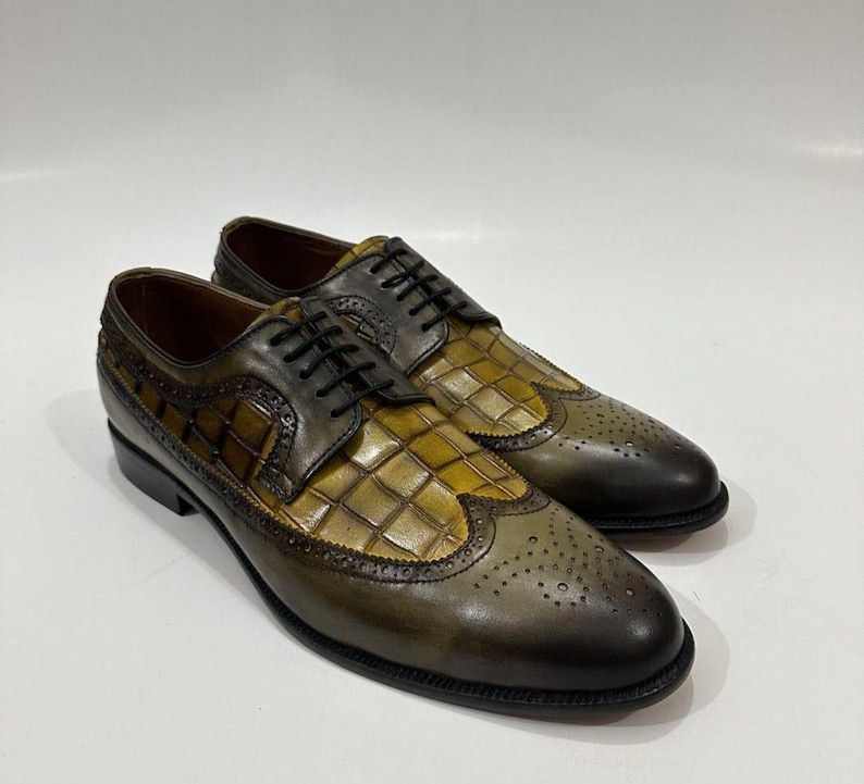 Puede incluir: Un par de zapatos oxford de cuero en color verde oliva y marr&oacute;n con dise&ntilde;o de punta de ala, detalles brogue y un patr&oacute;n de relieve de cocodrilo en el empeine y los paneles laterales. Incluyen cordones negros y un acabado de cuero liso.