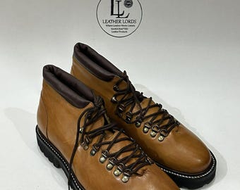 May include: Tan leather ankle boots featuring a dark brown padded collar, dark brown laces, and metal D-ring eyelets. The boots have a thick black lug sole with white stitching along the welt. A logo reads LEATHER LORDS.