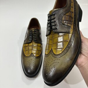 Puede incluir: Un par de zapatos tipo oxford con puntera decorada que presentan un dise&ntilde;o bicolor con un panel central de cuero en relieve de cocodrilo color amarillo mostaza y punteras y laterales de cuero marr&oacute;n oscuro bru&ntilde;ido, con cordones negros.