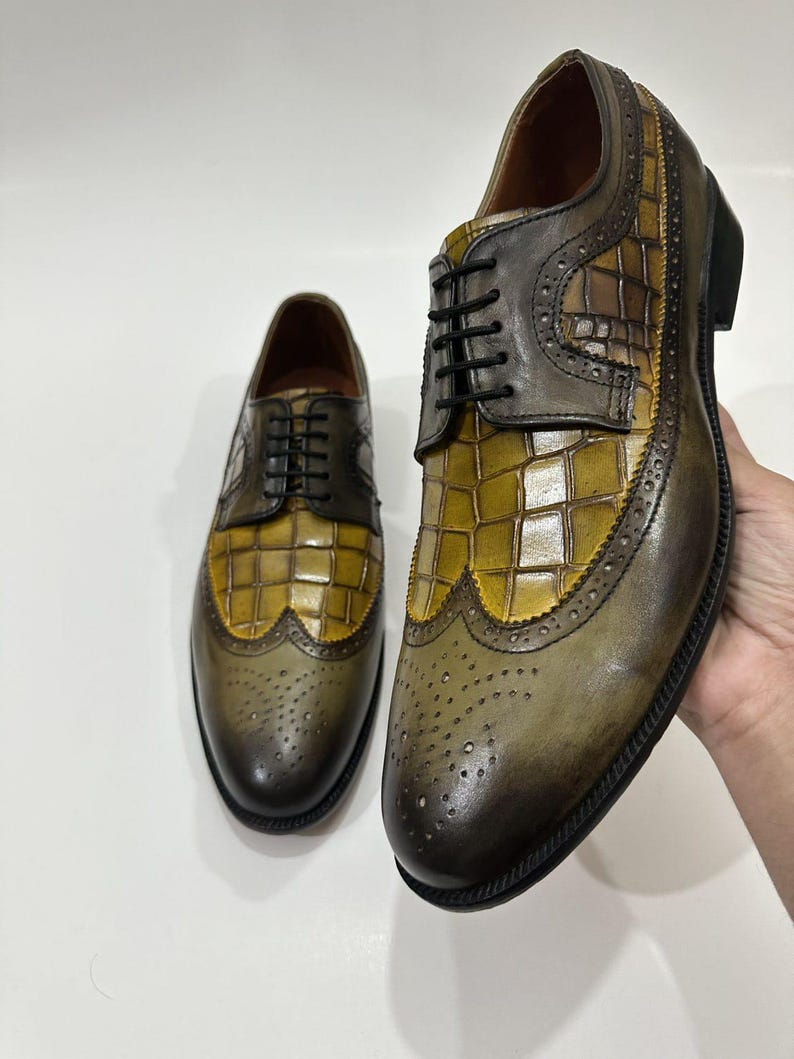 Puede incluir: Un par de zapatos tipo oxford con puntera decorada que presentan un dise&ntilde;o bicolor con un panel central de cuero en relieve de cocodrilo color amarillo mostaza y punteras y laterales de cuero marr&oacute;n oscuro bru&ntilde;ido, con cordones negros.