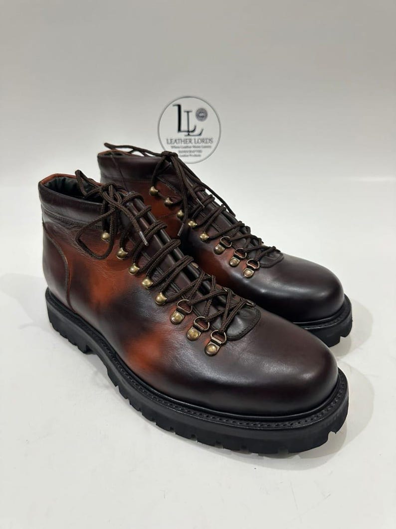 May include: A pair of dark brown leather ankle boots with a burnished finish, featuring dark brown laces, brass-toned metal eyelets, and a thick black lug sole. A circular logo with the text LEATHER LORDS is visible in the background.