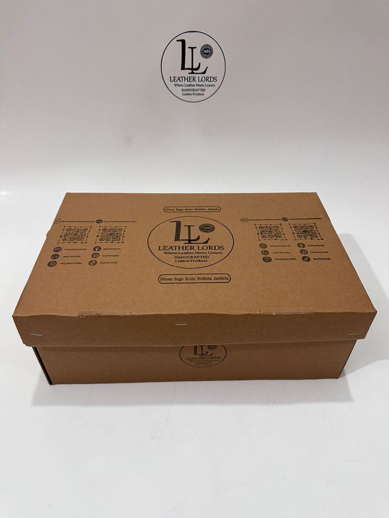 May include: A rectangular brown cardboard box featuring the black Leather Lords logo, text, and QR codes printed on the lid and front side. The branding includes the phrase Where Leather Meets Luxury and lists various leather products.