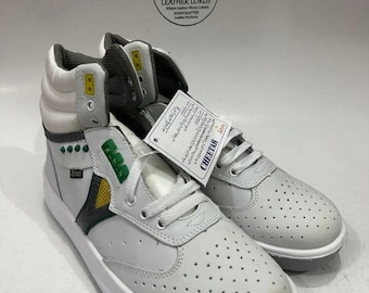 Könnte beinhalten: Paar weiße High-Top-Sneaker mit perforiertem Design. Die Sneaker haben graue und gelbe Akzente, weiße Schnürsenkel und eine weiße Sohle. Der Markenname "Cheetah" ist auf dem Etikett zu sehen.