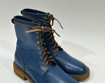 May include: A pair of blue leather lace-up boots featuring a smooth finish, brown laces, silver-toned metal eyelets, and a thick, textured brown rubber lug sole. The boots have a rounded toe and a pull tab at the back of the ankle collar.