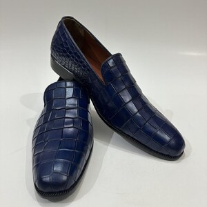 May include: A pair of navy blue slip-on loafers featuring a textured, embossed grid pattern across the upper surface. The shoes have a rounded toe, a low heel, and a smooth interior lining, showcasing a consistent deep blue color throughout.