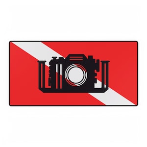 May include: A rectangular mouse mat with a black camera silhouette over a white diagonal stripe on a red background. The mouse mat has a black border and is designed for computer use.