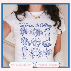 May include: A white t-shirt with the text "The Ocean Is Calling" in blue lettering. The shirt features a variety of blue illustrations of seashells, a lobster, a seahorse, an oyster, a crab, and seaweed.