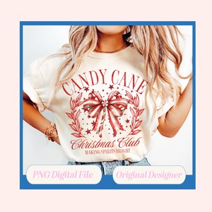 K&ouml;nnte beinhalten: Cremefarbenes T-Shirt mit einem rot-wei&szlig;en Zuckerstangen-Design. Die Grafik enth&auml;lt die Worte "CANDY CANE Christmas Club" und "MAKING SPIRITS BRIGHT". Das Design zeigt eine Zuckerstangen-Schleife, Sterne und Lorbeerbl&auml;tter.