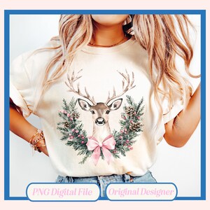 May include: Cream-colored t-shirt featuring a watercolor illustration of a deer with large antlers. The deer is surrounded by a wreath of pine needles, pink berries, and pine cones, with a pink bow at the bottom. The text "PNG Digital File" and "Original Designer" are at the bottom.