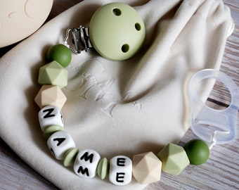 May include: A green and beige silicone baby teether with the name "NAME" spelled out in white letters. The teether is attached to a clip and comes with a white muslin bag.