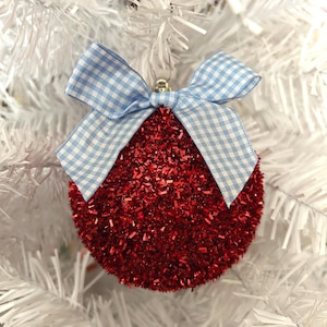 May include: A red sparkly Christmas ornament with a blue and white gingham bow.