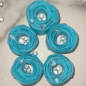 May include: Five blue paper rolls with clear rhinestones inside. The rolls are arranged in a circle on a white surface.