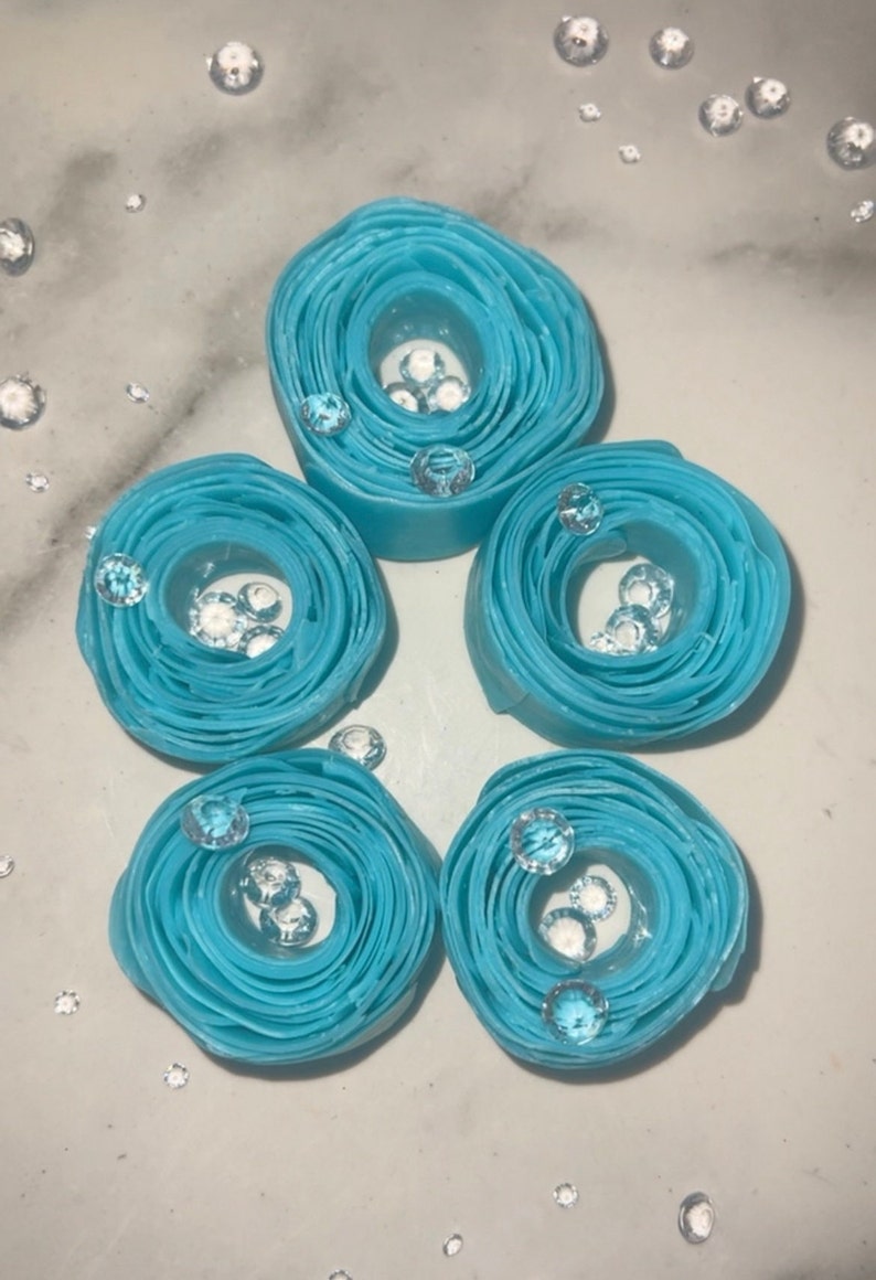May include: Five blue paper rolls with clear rhinestones inside. The rolls are arranged in a circle on a white surface.