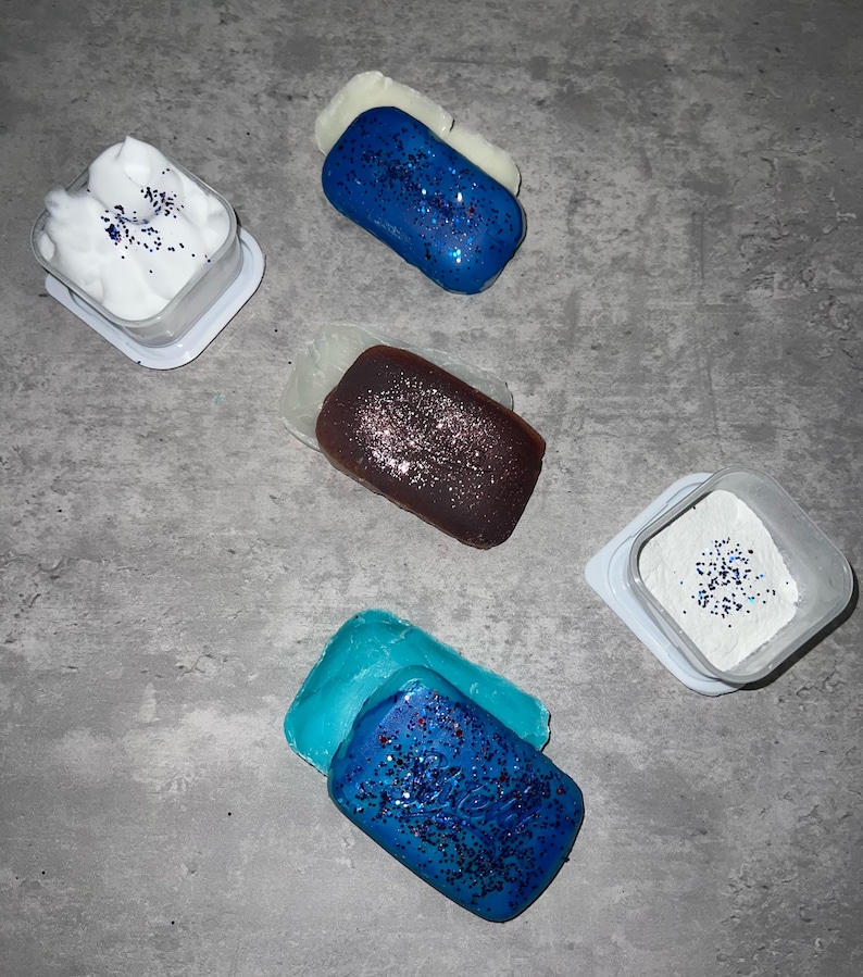 Puede incluir: Cuatro recipientes con tapas blancas y purpurina azul en el interior. Cada recipiente tiene una pastilla de jab&oacute;n a juego azul, morado o blanco con purpurina azul en la parte superior.