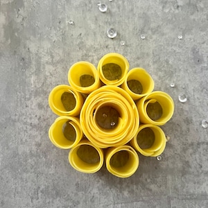 Puede incluir: Una flor de papel amarilla hecha de círculos de papel enrollados. La flor está sobre un fondo gris.