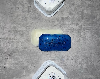 May include: Three containers with white powder and blue glitter. The top container has a fluffy white substance, the middle container has a solid blue bar, and the bottom container has a fine white powder.