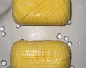 May include: Two yellow bars of soap with a grid pattern on the surface. The soap is on a white background.