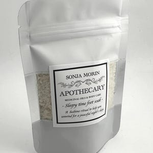 Puede incluir: Una bolsa blanca resellable con una etiqueta blanca que dice "SONJA MORIN APOTHECARY MEDICINAL OILS & BODY CARE - Sleepy time foot soak - A bedtime ritual to help you unwind for a peaceful night's sleep"