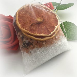 May include: A white mesh bag filled with bath salts and dried orange slices. The bag is tied with a white string.