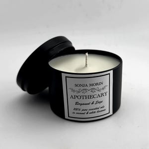 May include: A black candle jar with a white label that reads "SONJA MORIN APOTHECARY Bergamot & Sage 100% pure essential oils in coconut & white beeswax".