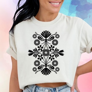 Könnte beinhalten: Ein weißes T-Shirt mit einem schwarzen Blumendesign. Das Design ist symmetrisch und enthält Blumen und Blätter.